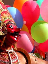 Javanese mask against a backdrop of brightly colored balloons.