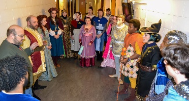 A group of actors stand together backstage doing a vocal warmup.