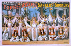 Show poster for Yorke and Adams' "Bankers and Brokers." The poster depicts women in Egyptian clothing standing in three rows. The ones at the front sit on the ground. There is a women who stands in the center with her arms extended slightly up and out to the sides as she holds the ends of her dress train, making the fabric fall behind her.