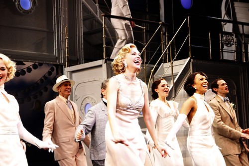 Image from the Broadway show "Anything Goes." Actors stand in a group wearing 1930s evening wear of light colors.